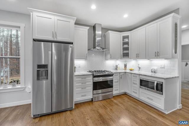 kitchen with white cabinetry, light wood finished floors, wall chimney exhaust hood, and appliances with stainless steel finishes