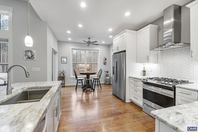 kitchen with light wood-style flooring, appliances with stainless steel finishes, white cabinetry, wall chimney exhaust hood, and a sink