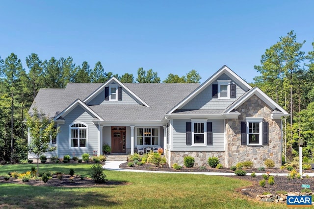 craftsman-style home featuring stone siding, covered porch, roof with shingles, and a front lawn