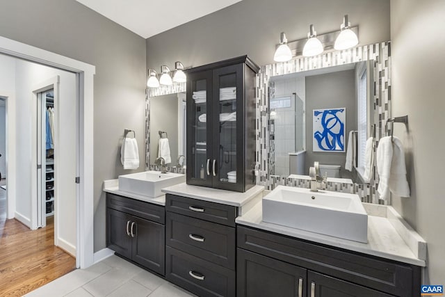 bathroom with a walk in closet, toilet, a shower stall, baseboards, and vanity