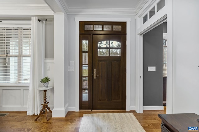 entryway with a healthy amount of sunlight, a decorative wall, wood finished floors, and ornamental molding