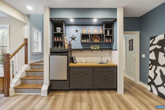 bar featuring light wood finished floors, stairway, indoor wet bar, refrigerator, and a sink