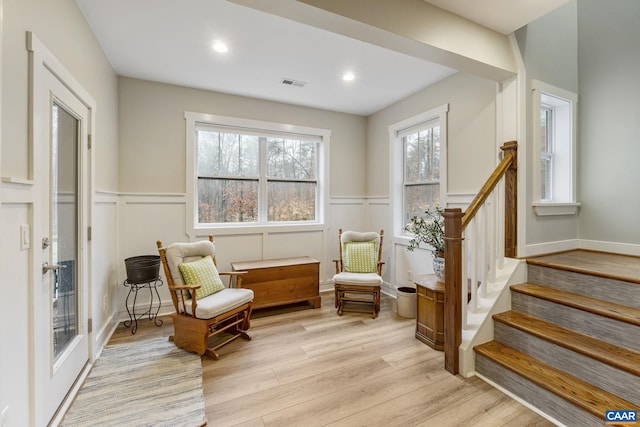 living area featuring stairway, visible vents, light wood finished floors, recessed lighting, and a decorative wall