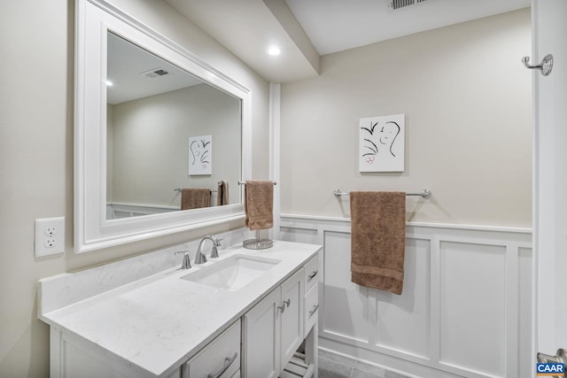 bathroom with visible vents, wainscoting, vanity, and a decorative wall