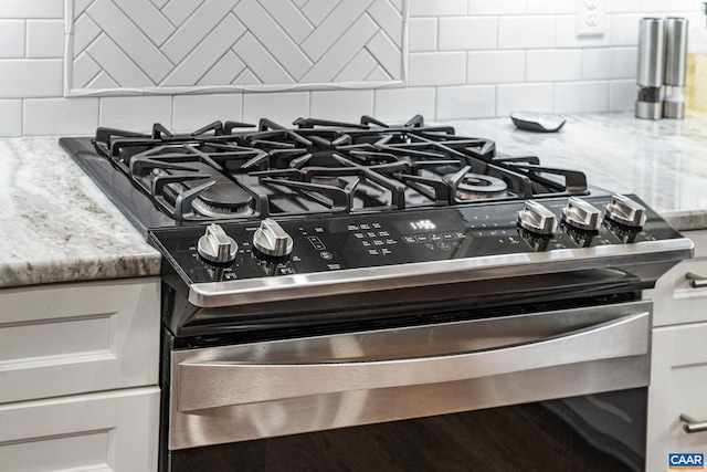 interior details with light stone counters, decorative backsplash, gas range, and white cabinetry