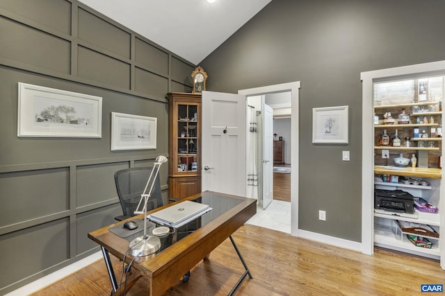 office featuring light wood-style flooring, a decorative wall, and high vaulted ceiling