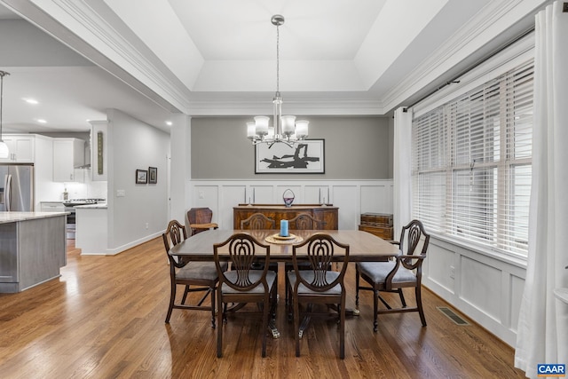 dining room with visible vents, light wood finished floors, a raised ceiling, a decorative wall, and a chandelier