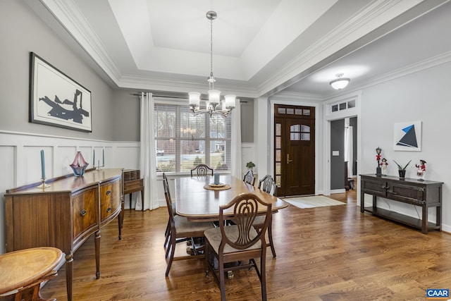 dining space featuring an inviting chandelier, a decorative wall, wood finished floors, and a raised ceiling