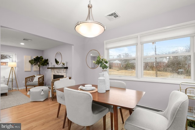 dining area featuring light wood-type flooring, a baseboard radiator, a premium fireplace, and visible vents