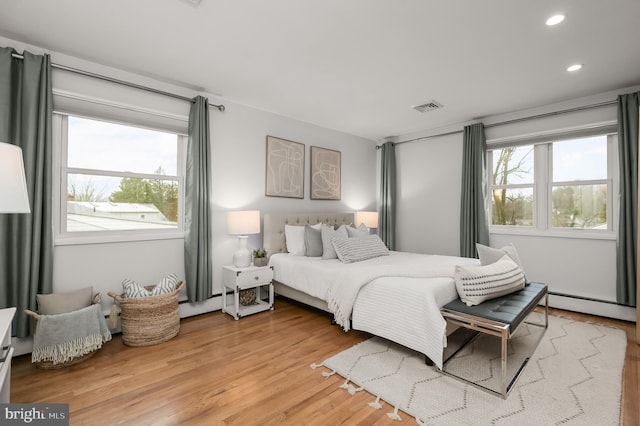 bedroom with light wood-style flooring, multiple windows, visible vents, and baseboard heating