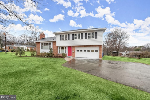 split level home featuring a chimney, aphalt driveway, an attached garage, a front lawn, and brick siding