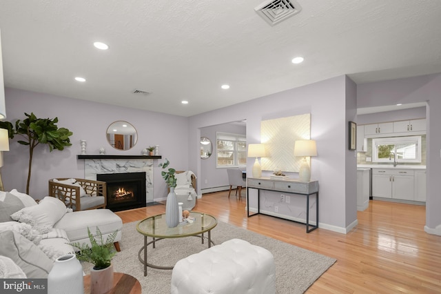 living area with a high end fireplace, a baseboard radiator, light wood-style flooring, and recessed lighting