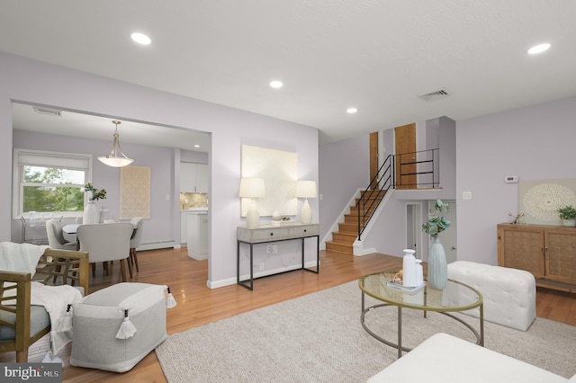 living area with visible vents, stairway, baseboard heating, and wood finished floors