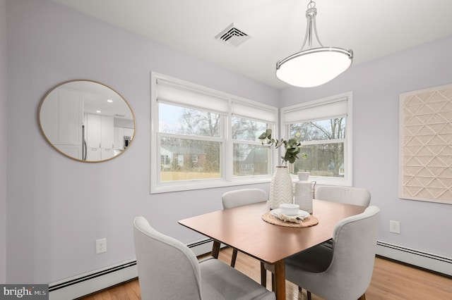 dining room featuring light wood-style floors, visible vents, and a baseboard heating unit