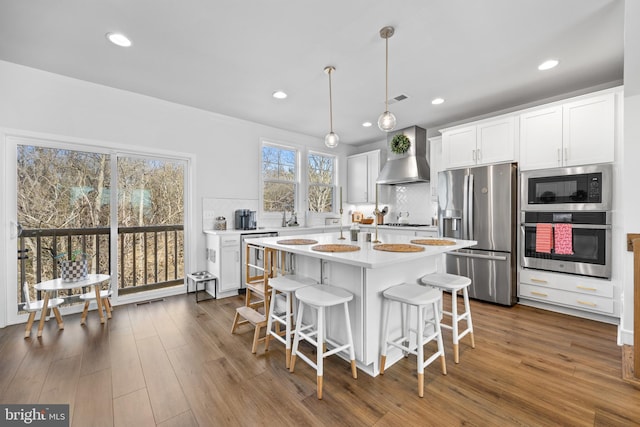 kitchen featuring dark wood-style floors, appliances with stainless steel finishes, backsplash, and wall chimney range hood