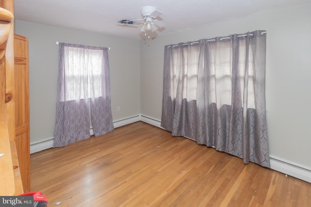 empty room featuring a ceiling fan, baseboard heating, and wood finished floors