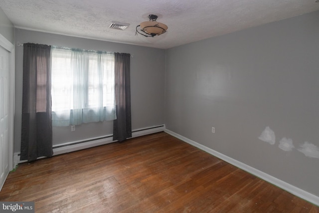 empty room featuring baseboards, visible vents, wood finished floors, baseboard heating, and a textured ceiling