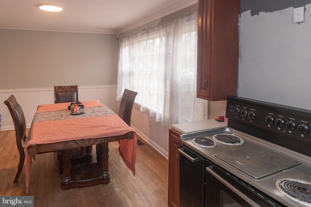 dining area with ornamental molding, a wainscoted wall, and light wood-style flooring