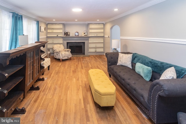 living area featuring ornamental molding, arched walkways, a fireplace, and wood finished floors