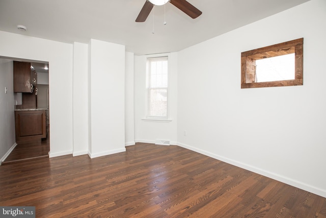 empty room with ceiling fan, visible vents, baseboards, and dark wood finished floors