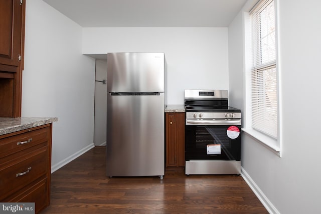 kitchen with dark wood-style floors, baseboards, appliances with stainless steel finishes, and light stone counters