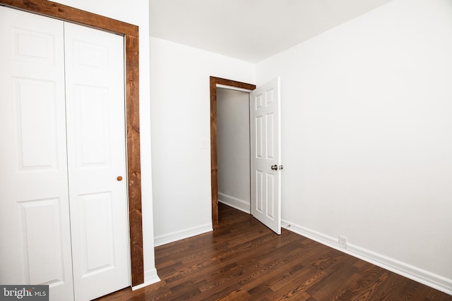 unfurnished bedroom with a closet, dark wood finished floors, and baseboards