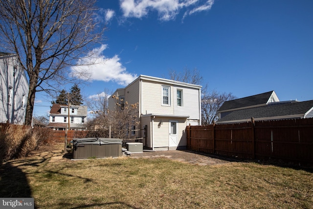 back of house with central AC, a fenced backyard, a lawn, and a hot tub