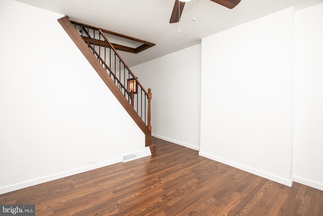 empty room featuring ceiling fan, wood finished floors, visible vents, baseboards, and stairway