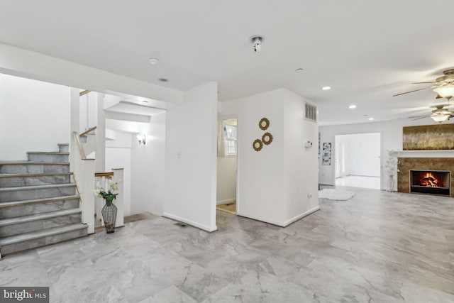 unfurnished living room featuring a warm lit fireplace, ceiling fan, recessed lighting, baseboards, and stairway