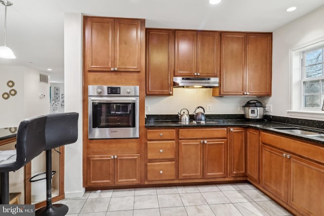 kitchen featuring under cabinet range hood, visible vents, brown cabinets, and oven