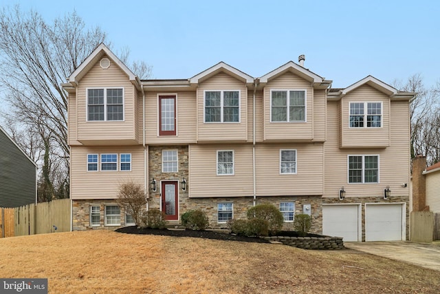 view of front of property with stone siding, an attached garage, fence, and driveway