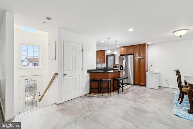 kitchen featuring a breakfast bar area, a peninsula, appliances with stainless steel finishes, brown cabinetry, and dark countertops