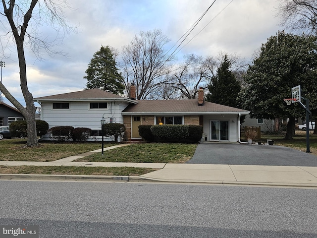 view of front of house featuring aphalt driveway, a chimney, and a front lawn