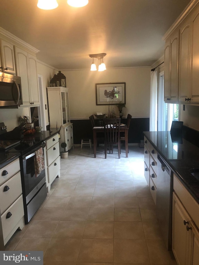 kitchen with light tile patterned floors, stainless steel appliances, ornamental molding, and dark countertops