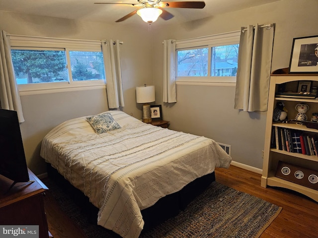 bedroom with a ceiling fan, visible vents, baseboards, and wood finished floors