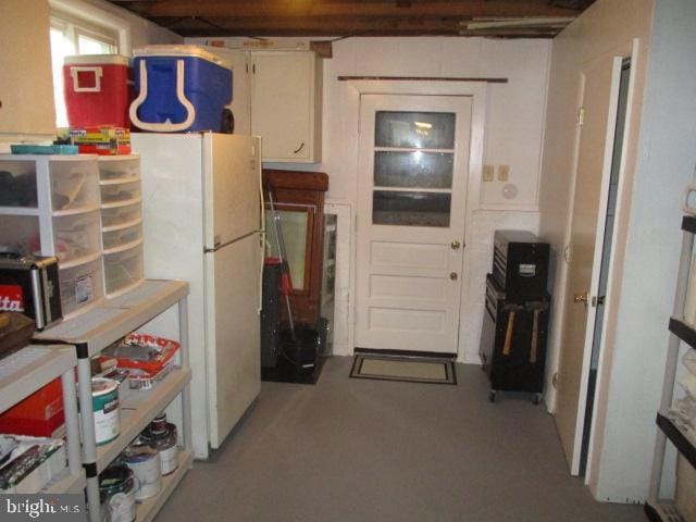 kitchen featuring concrete flooring, freestanding refrigerator, and white cabinets