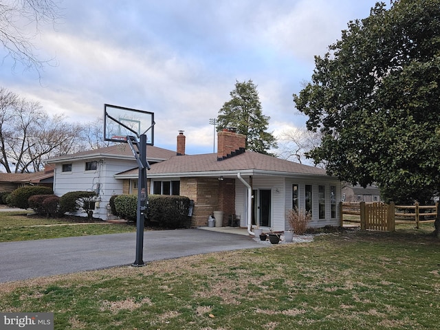 view of front facade with brick siding, fence, driveway, a front lawn, and a chimney