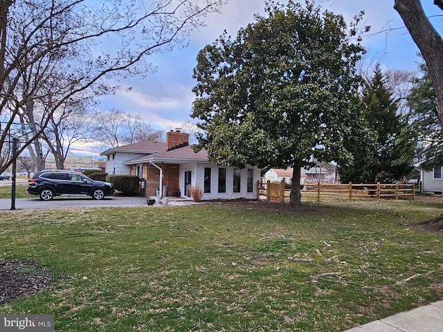 view of front of house featuring a front yard, brick siding, fence, and a chimney