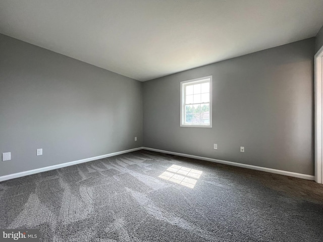 unfurnished room with baseboards and dark colored carpet