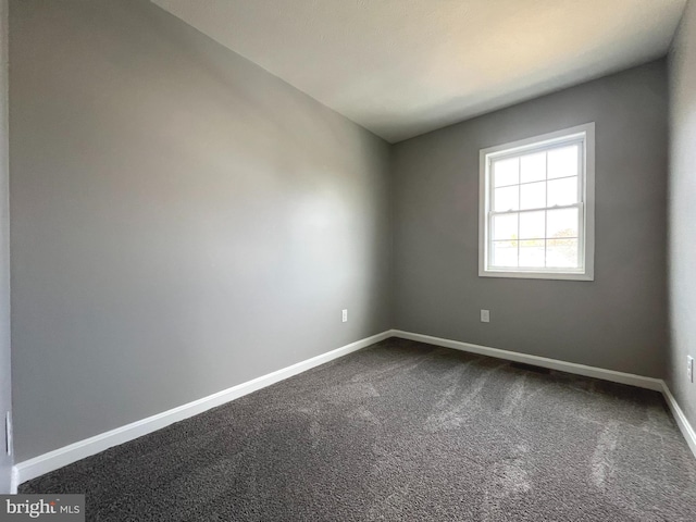 unfurnished room with baseboards and dark carpet