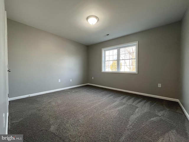 spare room featuring visible vents, baseboards, and dark colored carpet