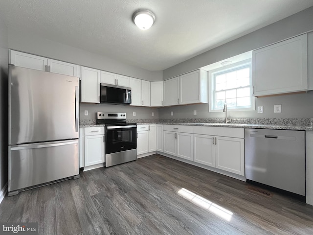 kitchen with a sink, dark wood finished floors, stainless steel appliances, white cabinets, and light stone countertops