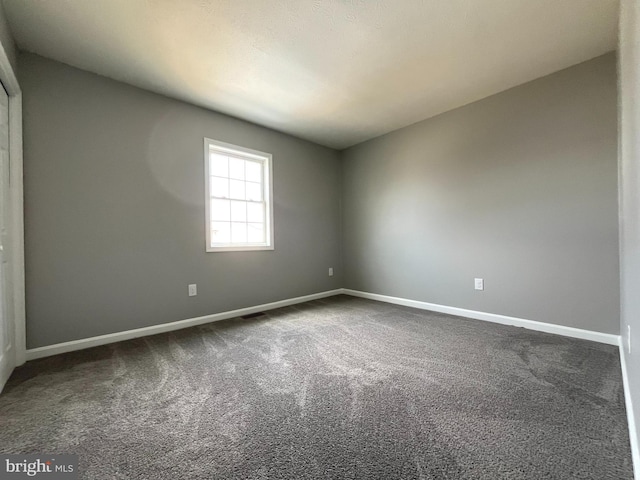 empty room with baseboards and dark colored carpet