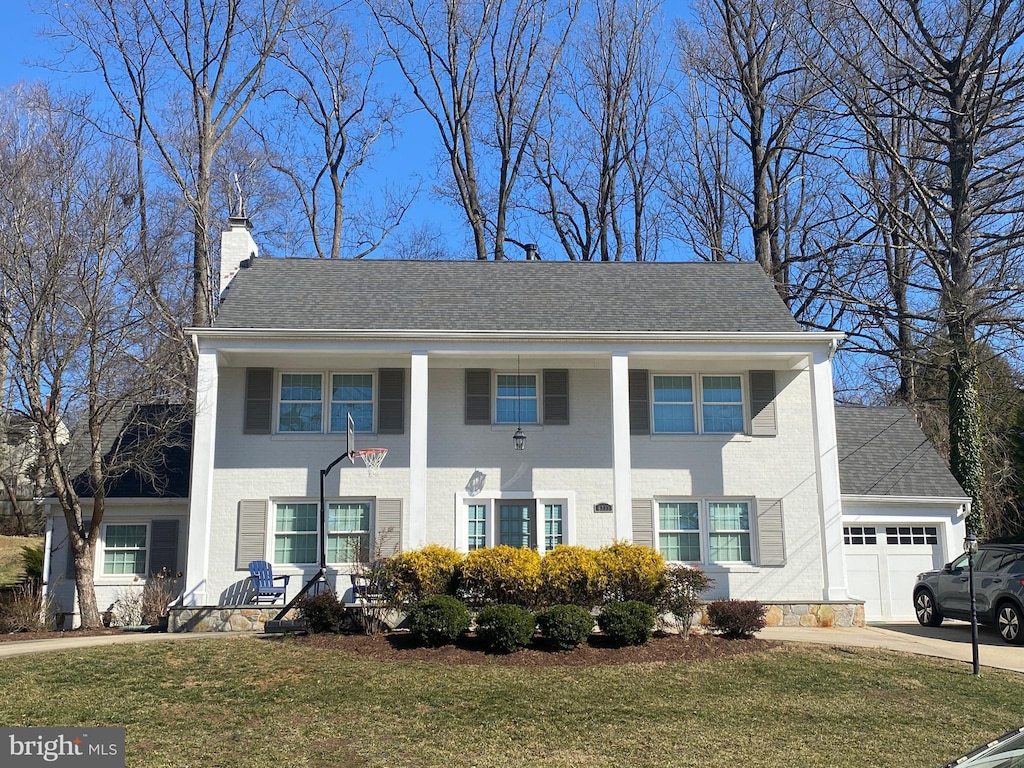 greek revival house with an attached garage, a shingled roof, concrete driveway, a chimney, and a front yard