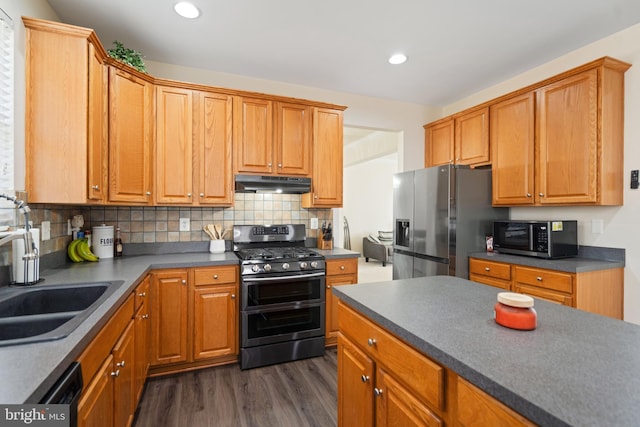 kitchen with dark countertops, tasteful backsplash, under cabinet range hood, stainless steel appliances, and a sink