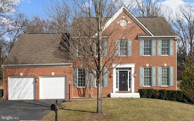 colonial-style house featuring brick siding, a front yard, an attached garage, and driveway