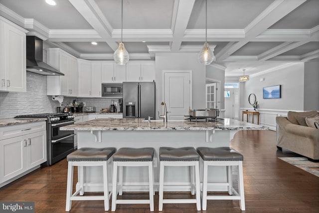 kitchen featuring wall chimney exhaust hood, appliances with stainless steel finishes, beamed ceiling, and a breakfast bar