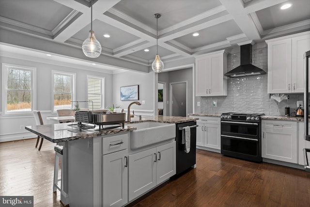 kitchen with stone countertops, range with two ovens, dishwasher, wall chimney exhaust hood, and a sink