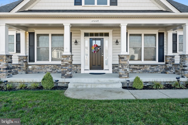 doorway to property featuring a porch, stone siding, and a shingled roof