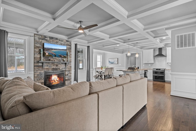 living room featuring a stone fireplace, dark wood-type flooring, coffered ceiling, visible vents, and beam ceiling